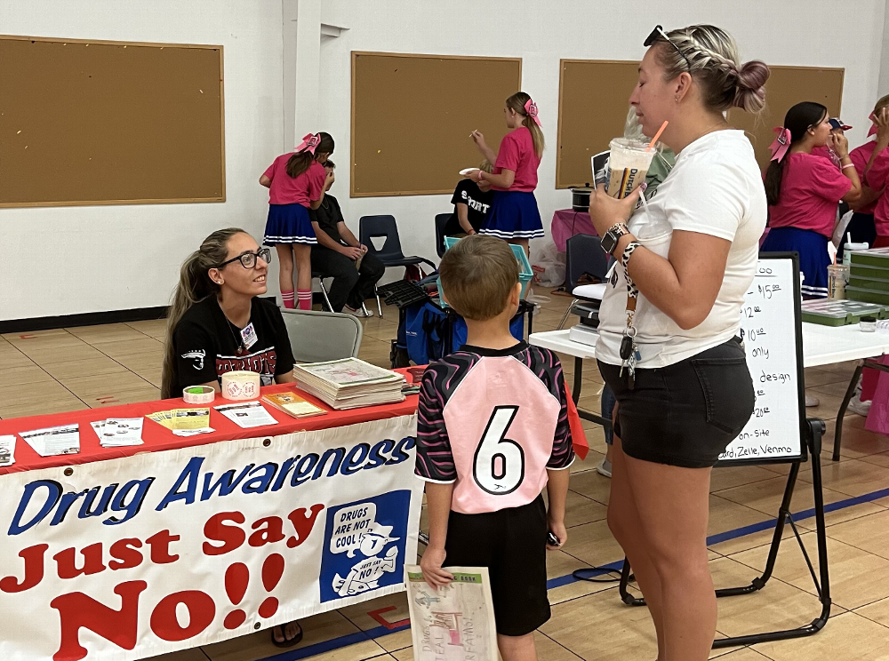 Drug Awareness Chairman  Sarah Valle speaking with car show attendees who are visiting her booth.